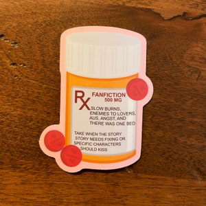 The image shows a sticker shaped like an orange and white medical pill bottle. The bottle is for the fantiction genre in books, movies, television, and other forms of media. The design is accented with red and pills with hearts on it. The text reads- Fanfiction 500mg. 
Slow burns, enemies to lovers, AUs, angst, and there was one bed. 
Take when the story needs fixing or specific characters should kiss.