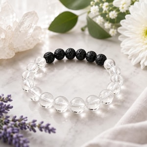 May include: A stretch bracelet featuring a series of clear, smooth, spherical beads alternating with a section of six porous, black, textured volcanic rock beads arranged in a circular pattern on a flexible cord for easy wear.