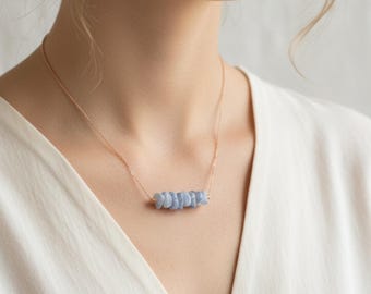 May include: A delicate necklace featuring a thin rose gold chain and a horizontal row of small, tumbled light blue lace agate stones. The stones are arranged side-by-side, creating a textured, organic focal point against the metallic chain.