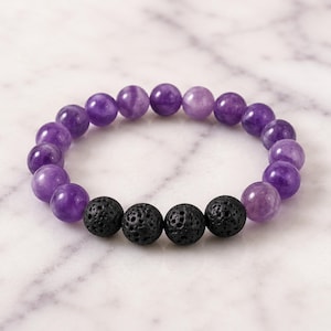 May include: A stretch bracelet featuring a series of smooth, round, translucent purple beads interspersed with four textured, porous, matte black lava beads. The beads are arranged in a circular pattern, creating a continuous loop of alternating colours.