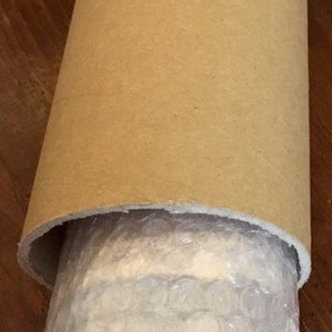 Puede incluir: Un tubo de cart&oacute;n marr&oacute;n con un forro de pl&aacute;stico de burbujas blanco en el interior. El tubo est&aacute; enrollado y el pl&aacute;stico de burbujas es visible.