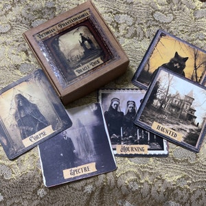 May include: A set of Victorian Phantasmagoria Oracle Deck cards featuring illustrations of a corpse, a spectre, mourning figures, a haunted house, and a wolf. The cards are brown with gold accents and feature gothic-inspired imagery.
