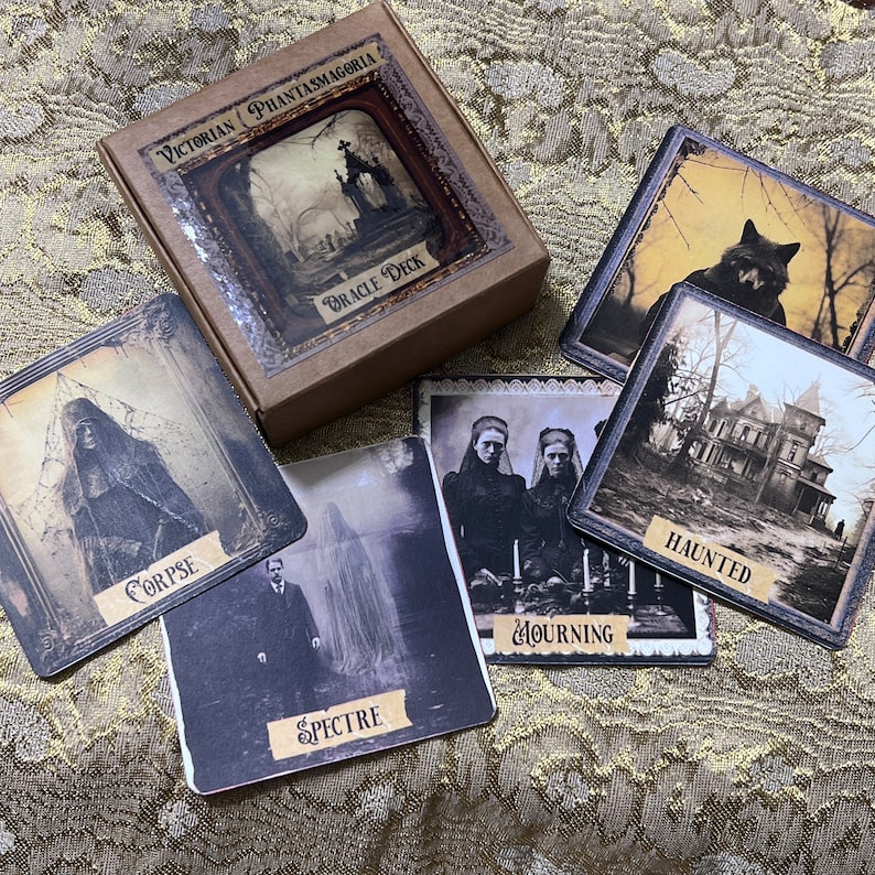May include: A set of Victorian Phantasmagoria Oracle Deck cards featuring illustrations of a corpse, a spectre, mourning figures, a haunted house, and a wolf. The cards are brown with gold accents and feature gothic-inspired imagery.