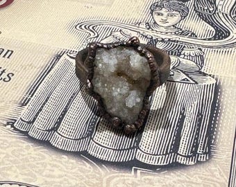 May include: A copper ring with a large, white, crystal-like stone set in the center. The stone has a rough, natural texture.