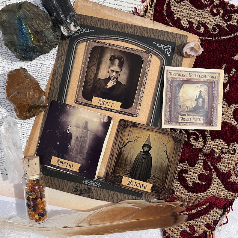 May include: A vintage-style tarot deck with four cards displayed. The cards are titled "Secret", "Spectre", "Watcher", and "Oracle Deck". The cards are on a brown surface with a feather and a small bottle of amber stones.