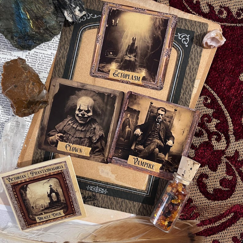May include: A vintage-style oracle deck with a dark, gothic aesthetic. The cards feature illustrations of a clown, a vampire, and an ectoplasm. The box is labeled "Victorian Phantasmagoria Oracle Deck".