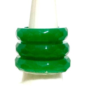 以下が含まれることがあります： 白いディスプレイスタンドに重ねられた、3つのファセット加工されたエメラルドグリーンのリング。リングは光沢のある仕上げと幾何学的なデザインです。背景は無地の白で、リングの鮮やかな緑色を際立たせています。