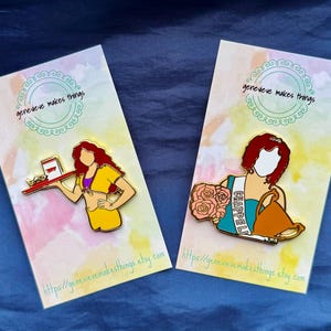May include: Two enamel pins featuring a woman in a yellow outfit holding a tray of food and a woman in a blue dress with a sash that says "Chippendale" holding a golden trophy. The pins are on white cards with the text "genevieve makes things" and a website address.