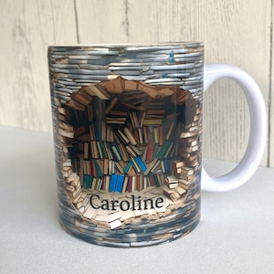 May include: White ceramic mug with a personalized name "Caroline" printed on the bottom. The mug features a graphic of a wall of books with a hole in the middle, revealing a stack of books.