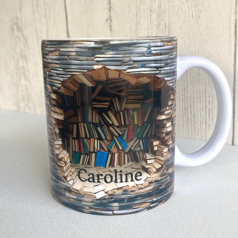May include: White ceramic mug with a personalized name "Caroline" printed on the bottom. The mug features a graphic of a wall of books with a hole in the middle, revealing a stack of books.