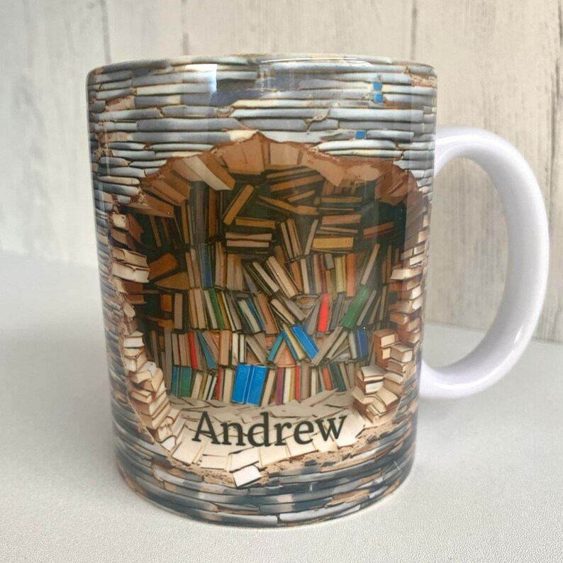 May include: White ceramic mug with a colorful image of a wall of books with a hole in the middle. The name "Andrew" is printed on the bottom of the hole.