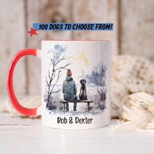 May include: White ceramic mug with a red handle. The mug features a watercolor illustration of a person and a dog sitting on a bench in a snowy landscape. The text "Rob & Dexter" is printed on the bottom of the mug.