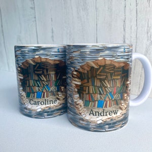 May include: Two white ceramic mugs with a colorful image of a bookshelf filled with books. The mugs have the names "Caroline" and "Andrew" printed on them.