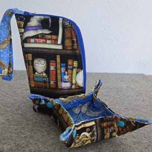 May include: A blue and brown fabric dice tray with a zippered pouch. The pouch has a print of bookshelves with owls, potions, and a witch's hat. The tray has a similar print with owls and stars.