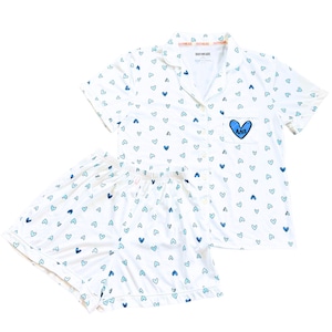 May include: White pajama set with a pattern of blue hearts. The short-sleeved top has a breast pocket with a blue heart and Greek letters. The shorts have an elastic waistband. The set is made of a lightweight fabric.
