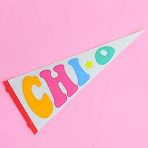 May include: A white felt pennant with the word "CHIO" in colorful felt letters. The letters are orange, pink, blue, and green. There is a yellow star between the "I" and "O".
