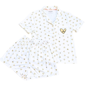 May include: White pajama set with a pattern of small gold hearts. The set includes a short-sleeved button-up shirt and matching shorts. The shirt pocket features a yellow heart with the letters "KAD". The brand name "DIRTY HEADS" is printed on the collar.
