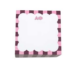 May include: A stack of pink and dark purple checkered notepads. The notepad has a white cloud-shaped border and the letters "AΦ" in pink. The notepads are stacked on top of each other.
