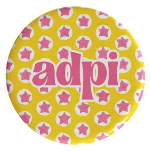 May include: A yellow button with pink stars and the word "adpi" in pink letters.