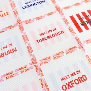 May include: A white fabric with a grid pattern featuring the text "Meet Me In" followed by various city names in pixelated fonts. The words "DUOTHREADS" are repeated diagonally across the design in orange and pink.