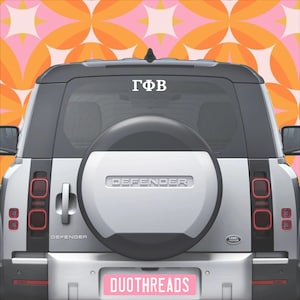May include: Rear view of a silver SUV with a spare tire. The vehicle has a white decal with Greek letters on the rear window. A pink license plate with the text "DUOTHREADS" is visible.