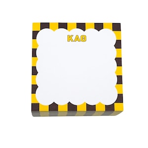 May include: A stack of square sticky notes with a yellow and brown checkered border. The center has a white scalloped edge and the word "KAO" in yellow letters.