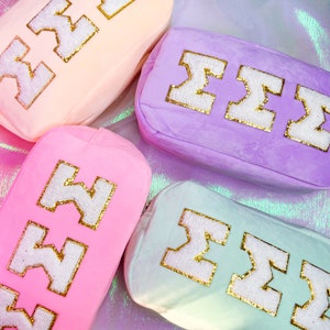 May include: Four plush cosmetic bags in different pastel colors with the Greek letter Sigma embroidered in white with gold glitter trim.