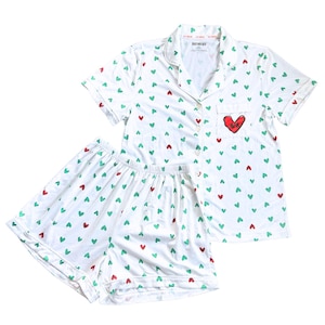 May include: White pajama set with a pattern of green and red hearts. The short-sleeved top has a red heart with the word "Love" embroidered on the pocket. The shorts have an elastic waistband. The brand name "OUTTHREDS" is printed on the collar.