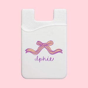 May include: White phone grip with a purple and yellow bow and the name "Lphie" written in purple.