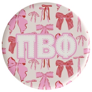 May include: A white button with a pink and red bow pattern and the letters "TBO" in white with a pink outline.