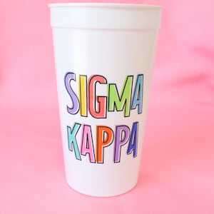 May include: White plastic cup with the words "SIGMA KAPPA" printed in colorful letters.