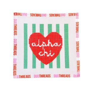May include: A square needlepoint canvas featuring a red heart with the white text alpha chi centered over vertical green stripes. The border is printed with the repeating text DUOTHREADS in alternating pink and orange colors on all sides.