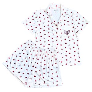 May include: White pajama set with a red heart pattern. The short-sleeved top has a collared neckline and a pocket with a heart design. The matching shorts complete the set. The text "Sweet Dreams Kids" is visible on the top.