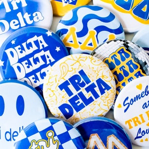 May include: A collection of colorful, patterned, and textured round stickers with the text "Tri Delta" in blue letters on a white background. The stickers are arranged in a circular pattern.