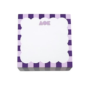 May include: A square notepad with a purple and white checkered pattern border. The notepad has a white, scalloped-edge area for writing, with the Greek letters ΔΦΕ in purple at the top.