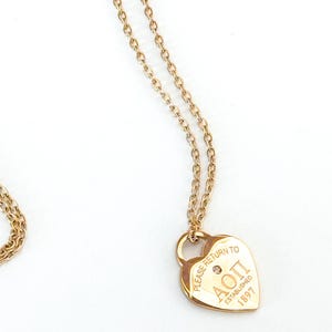 May include: A gold-colored necklace with a heart-shaped pendant. The pendant has the text "PLEASE RETURN TO AOII ESTABLISHED 1897" and a small diamond. The necklace chain is delicate and gold-toned.