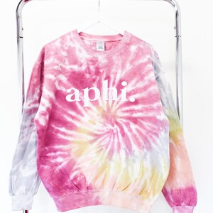 May include: A pink, yellow, and gray tie-dye sweatshirt with the word "aphi" printed in white on the front.
