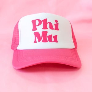 May include: A pink and white trucker hat with the words "Phi Mu" in pink letters on the front.