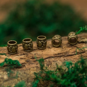 May include: Five antique gold-toned metal beads with a textured surface. The beads are arranged in a row on a wooden surface with green moss.
