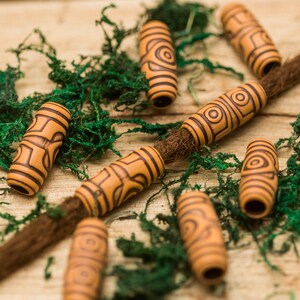 Könnte beinhalten: Nahaufnahme von braunen Holzperlen mit komplizierten Mustern. Die Perlen sind auf einer braunen Schnur aufgefädelt und auf einem grünen Moosuntergrund verstreut.