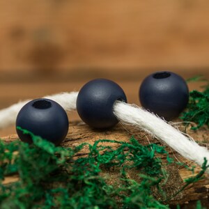 May include: Three dark blue wooden beads strung on a white cord, resting on a bed of green moss and a piece of brown wood.
