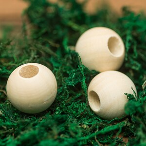 May include: Three natural wood beads with a hole through the center. The beads are sitting on a bed of green moss.