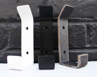 Puede incluir: Tres ganchos de pared de metal en diferentes acabados: blanco, negro y marrón rústico. Cada gancho tiene un diseño simple y curvo.