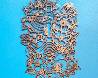 May include: A metal wall art piece in the shape of a human rib cage with floral designs. The piece is a light gold colour and is set against a bright blue background.