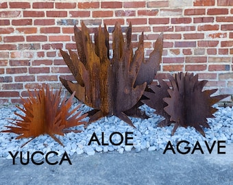 Puede incluir: Tres esculturas metálicas de plantas, que se asemejan al aloe, el agave y la yuca. Las esculturas están hechas de metal oxidado y tienen un aspecto natural y orgánico. Las esculturas están dispuestas sobre un lecho de grava blanca.