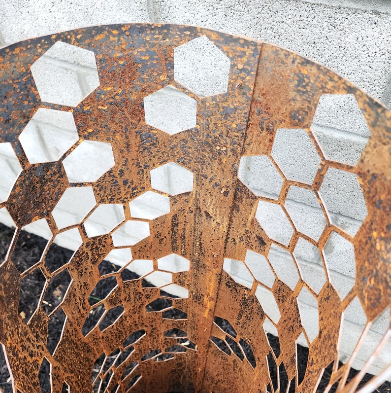 May include: A rusty metal fire pit with a hexagonal pattern cut out. The fire pit is made of thick metal and has a rustic look.