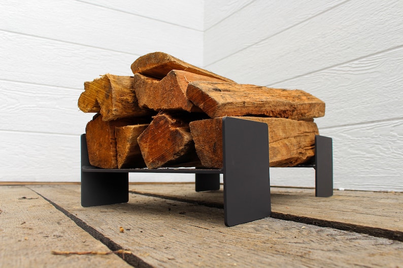 May include: A black metal firewood rack with a stack of firewood logs on top. The rack is sitting on a wooden deck.