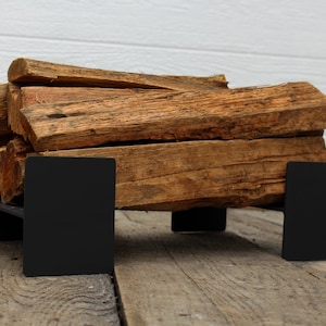 May include: A black metal firewood rack with stacked pieces of firewood on top. The rack is sitting on a wooden floor.