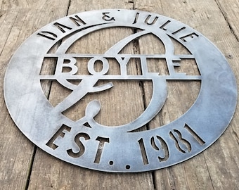 May include: A circular metal sign featuring the text "Dan & Julie Boyle Est. 1981" in a stylised font. The sign is a dark grey colour and has a rustic, industrial look.
