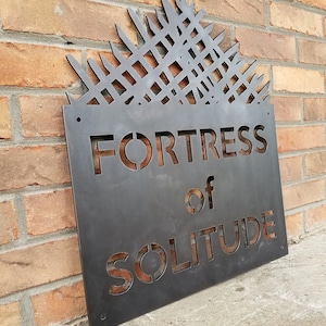 May include: A metal sign with a geometric design at the top and the words "Fortress of Solitude" in a stencil font.